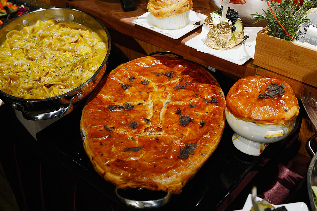 Assorted gourmet dishes on a wooden table, including a large round pie, and pasta in a glass bowl