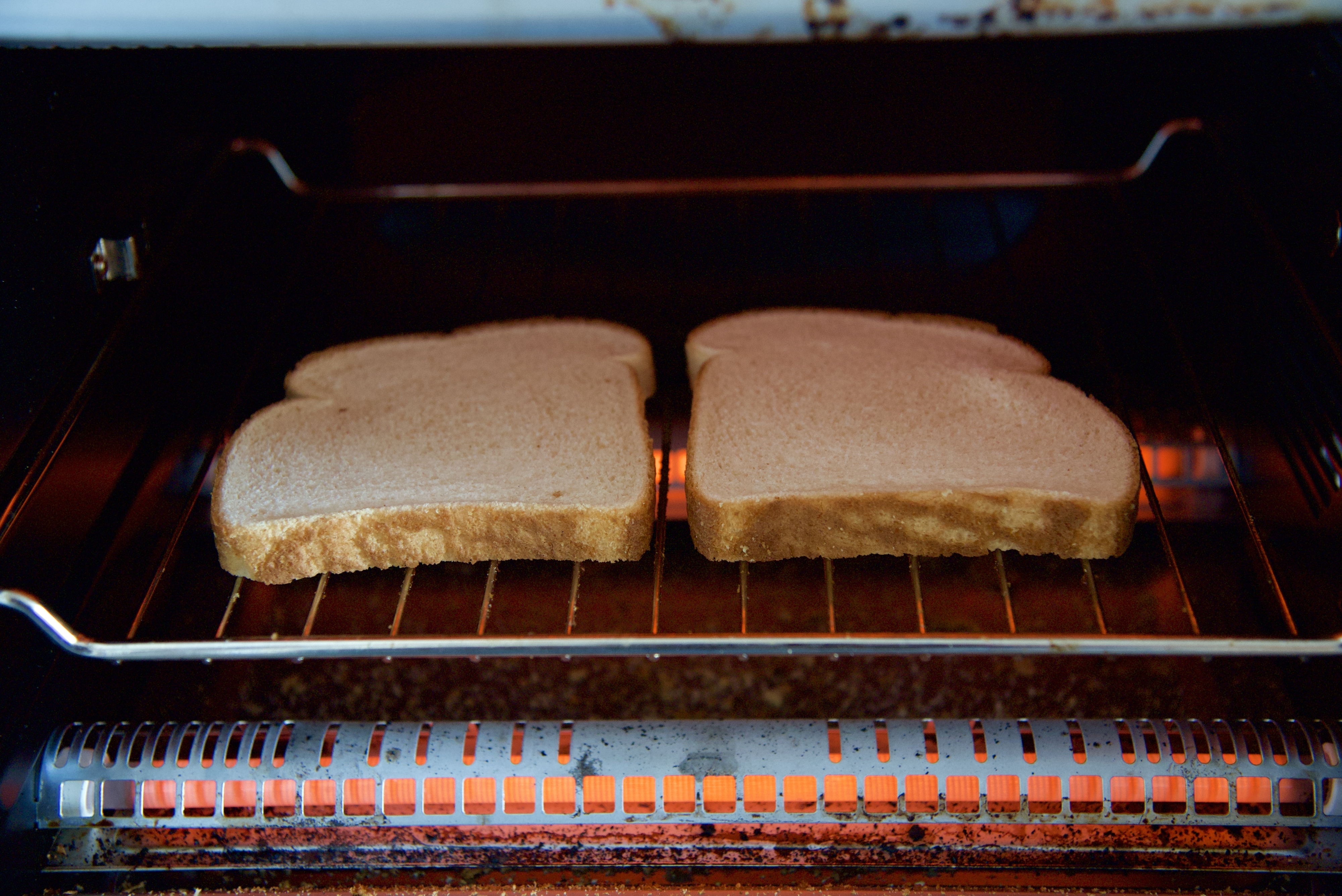 Two slices of bread toasting in an open toaster oven