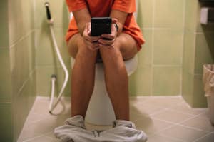 Person on toilet using smartphone, clothes at ankles