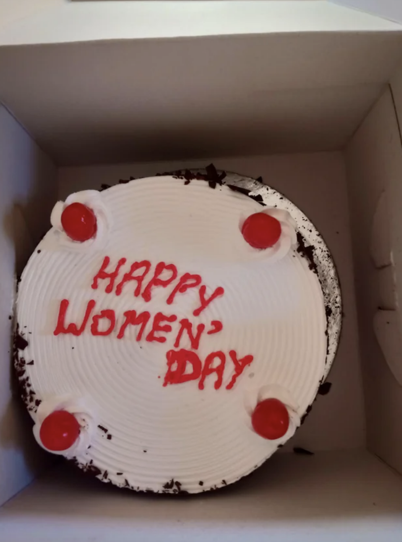 A cake with &quot;HAPPY WOMEN&#x27; DAY&quot; written on it erratically in icing, adorned with four cherries