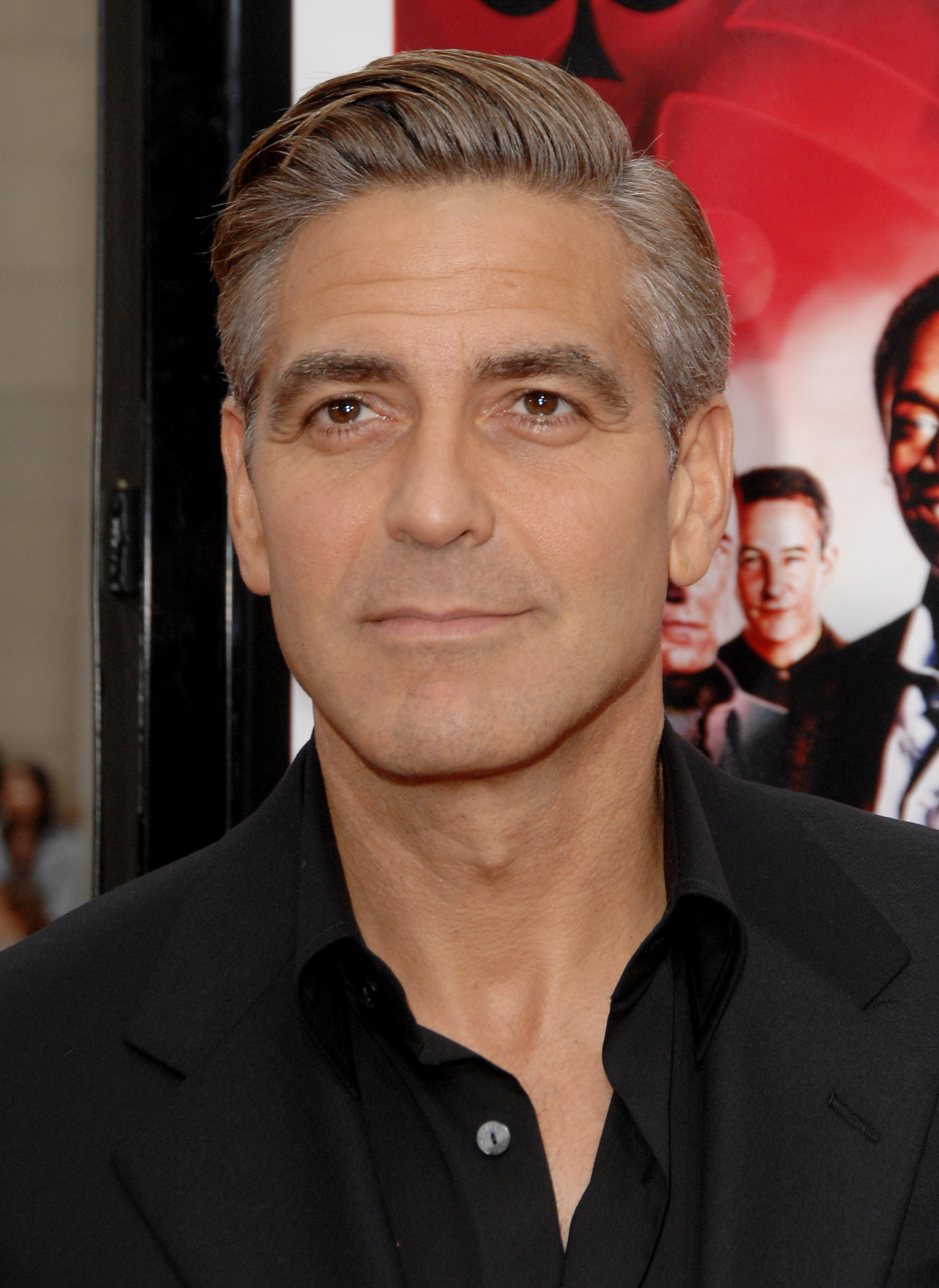 George Clooney wearing a black suit and open collared shirt at a premiere