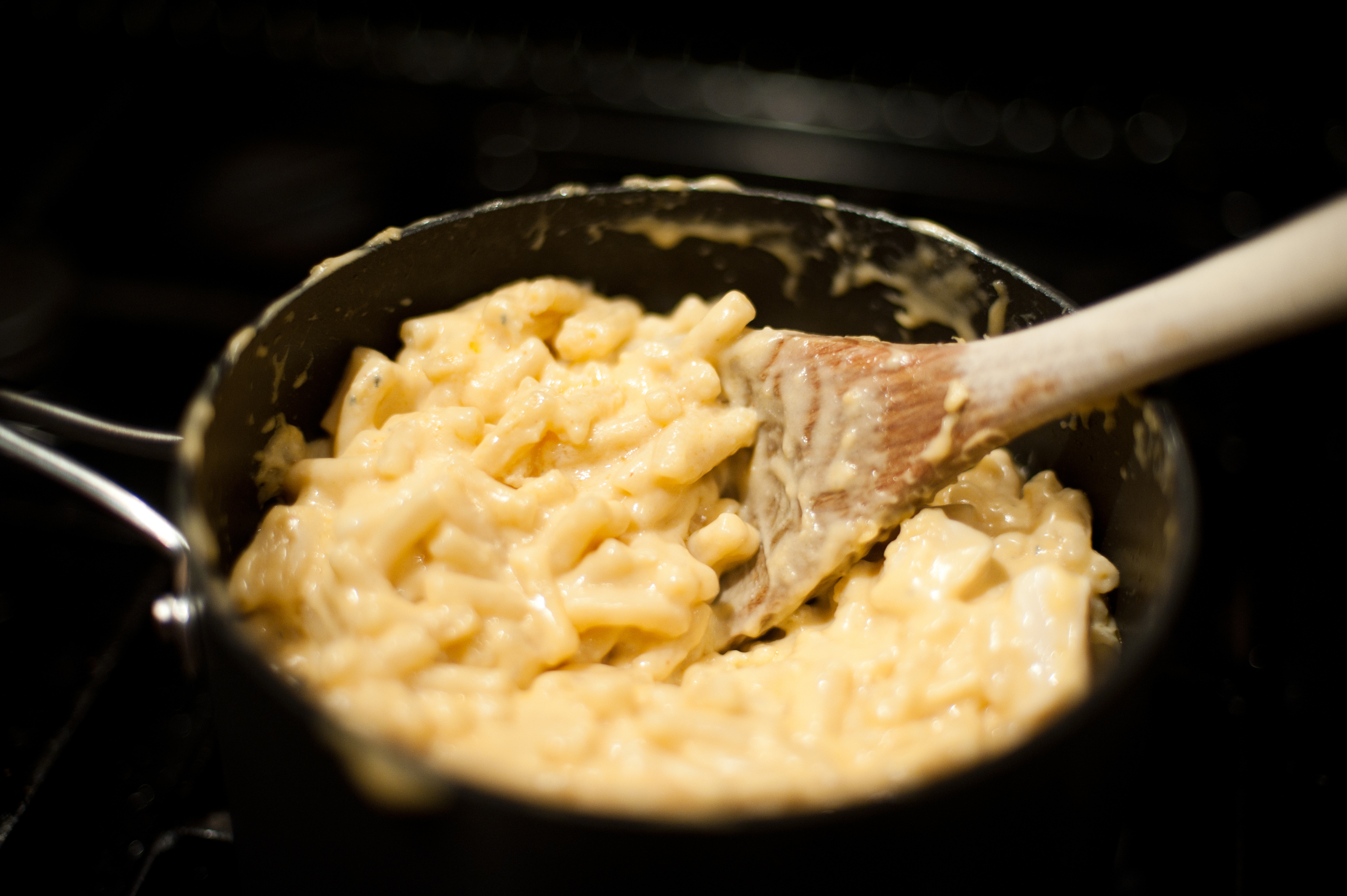 A pot of creamy macaroni and cheese being stirred with a wooden spoon