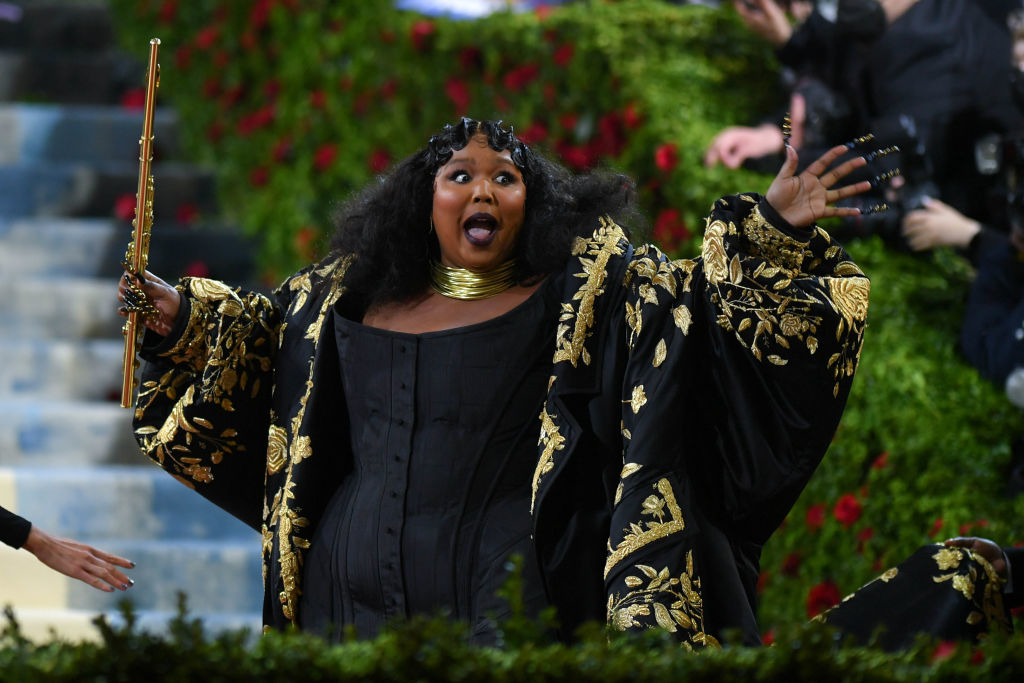 Lizzo in ornate  outfit holding a flute, gesturing excitedly