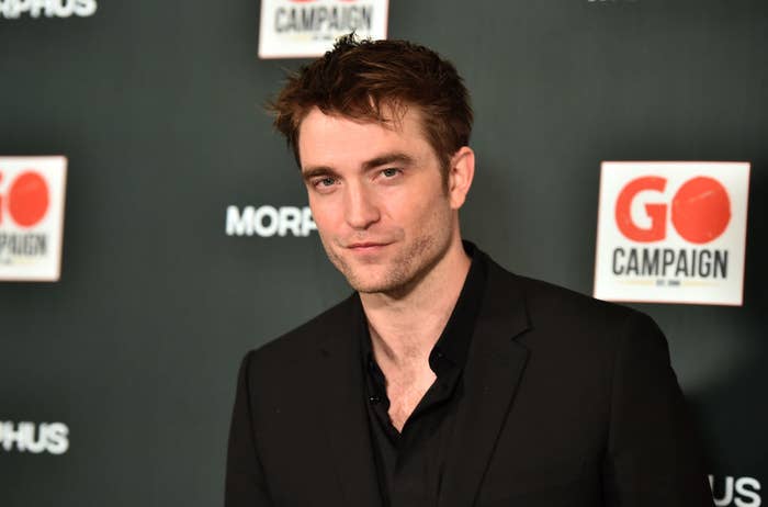Robert in a black suit posing at an event with sponsor logos in the background