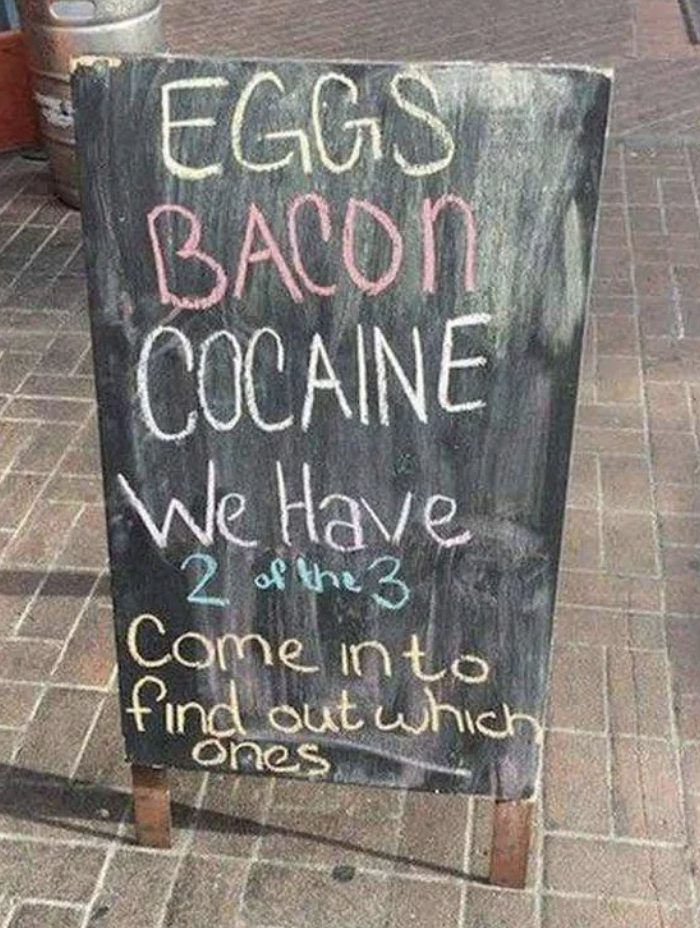 Signboard with humorous menu listing eggs, bacon, and a misspelled illicit substance, inviting to discover which two are available