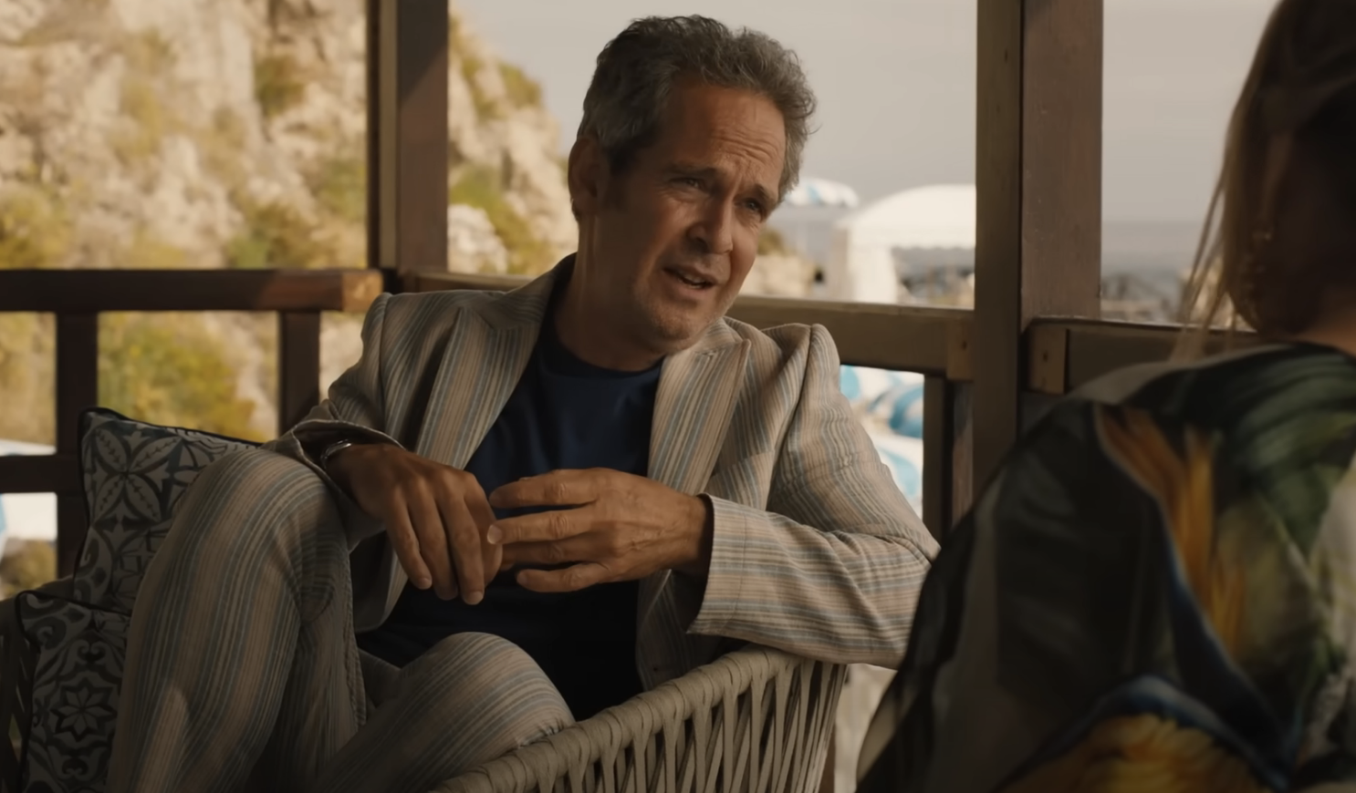 tom in a striped suit sits, conversing with an unseen character in a film scene