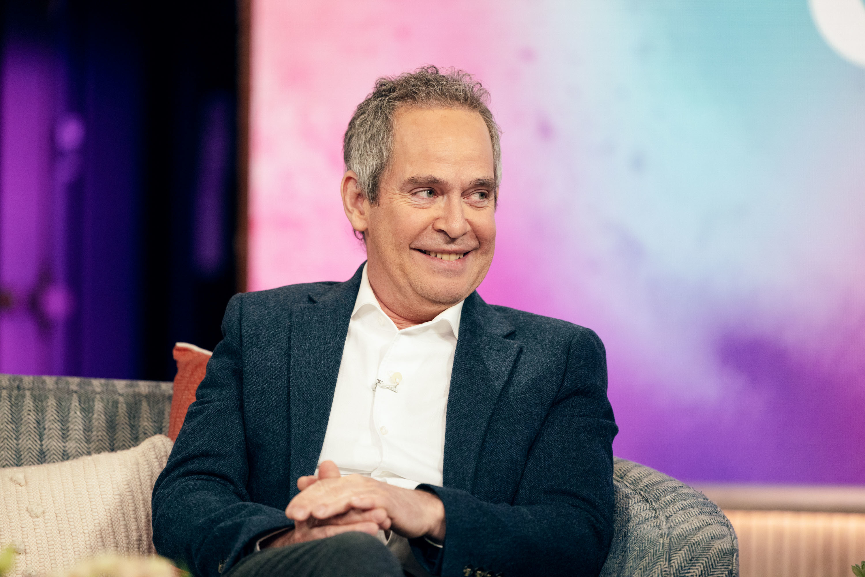 tom sitting, wearing a blazer with a shirt, smiling in an interview setting