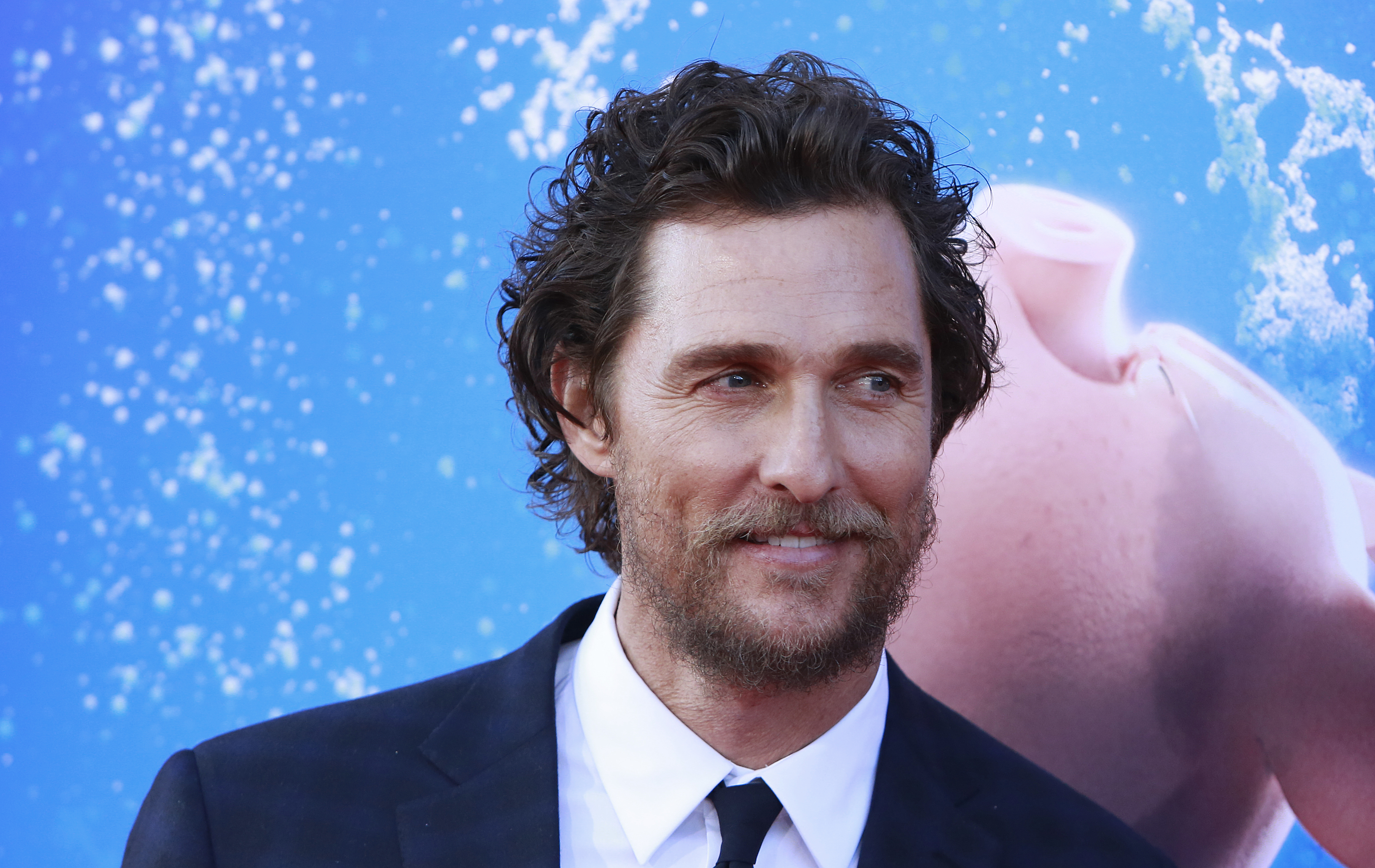 Matthew McConaughey in a suit at a movie premiere with a graphic backdrop