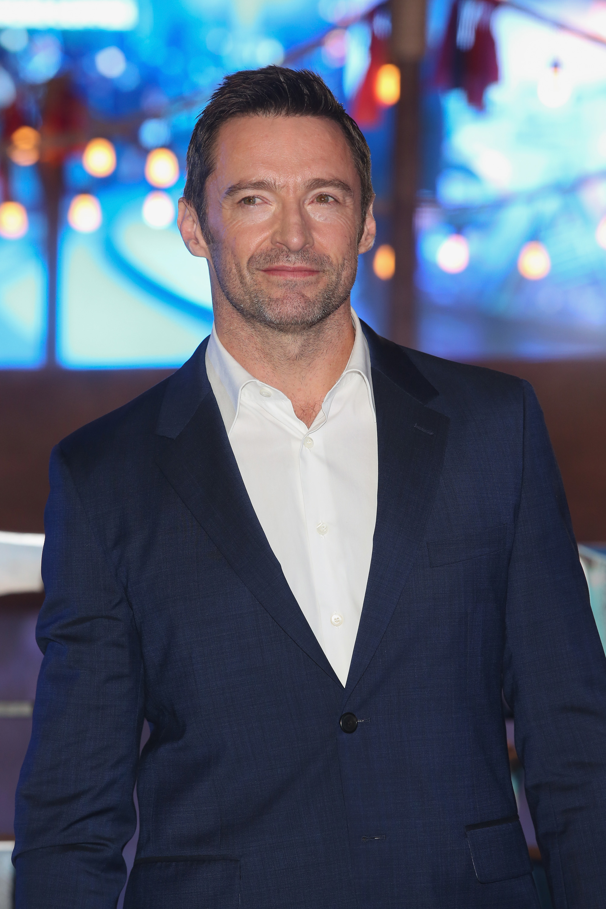 Hugh Jackman wearing a smart navy suit and smiling at a public event