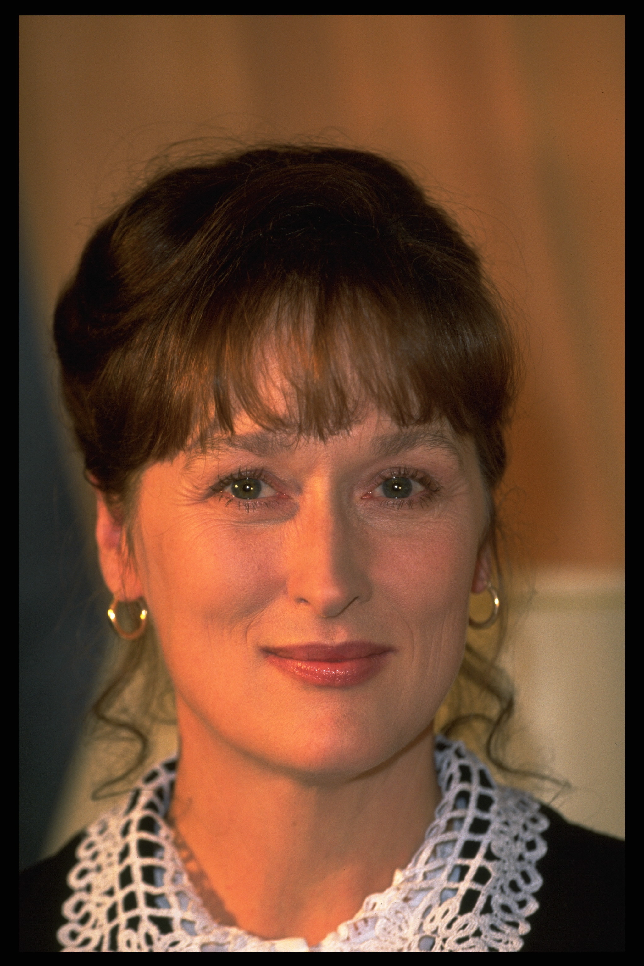 Close-up of Meryl Streep smiling in a lace-collared top and hoop earrings