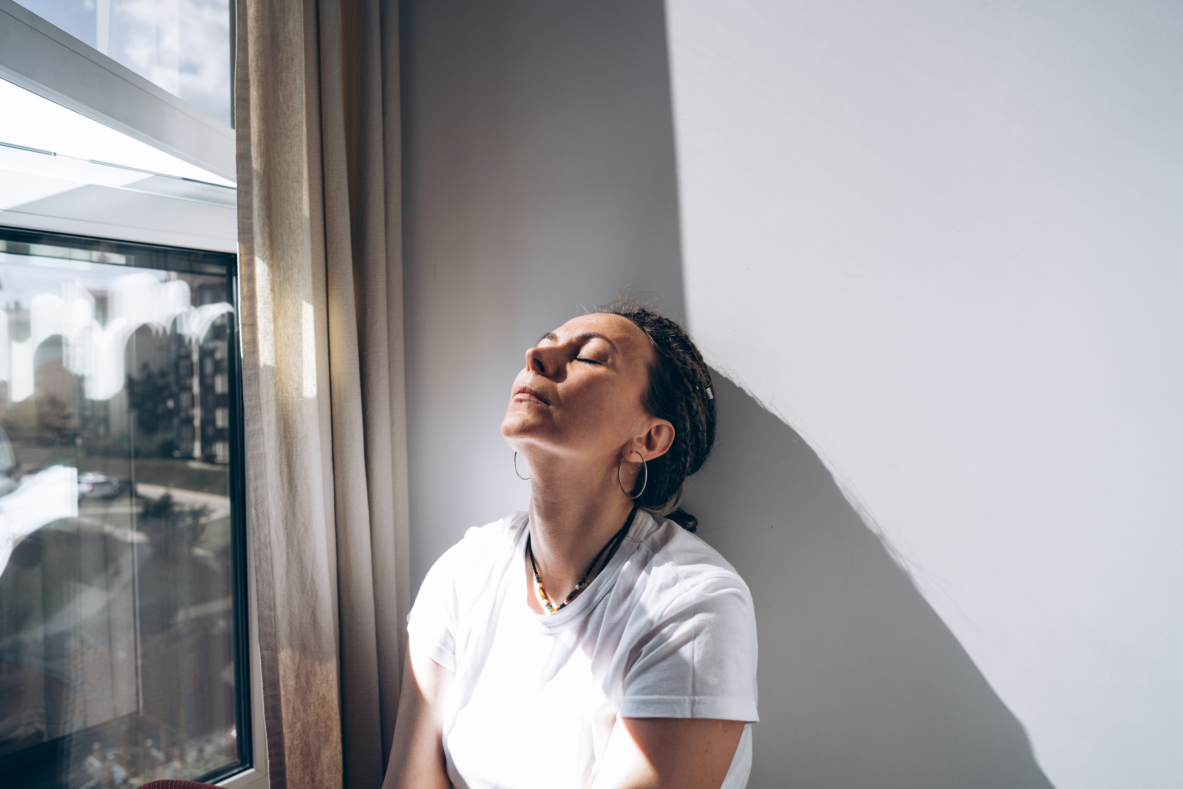 Person relaxing by a window with closed eyes and a content expression