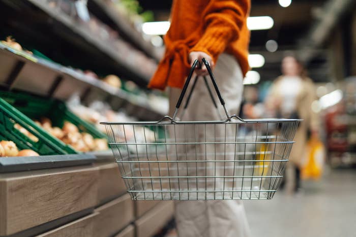 Person carrying an empty shopping basket in a grocery store aisle