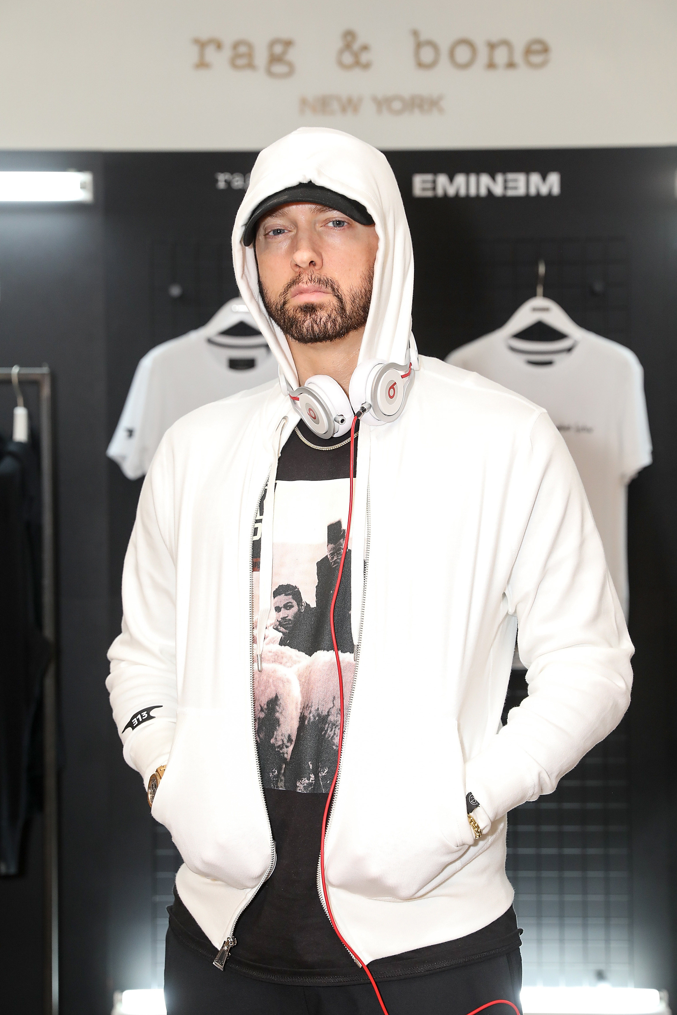 Eminem wearing a white hoodie and headphones in a store with his branded merchandise