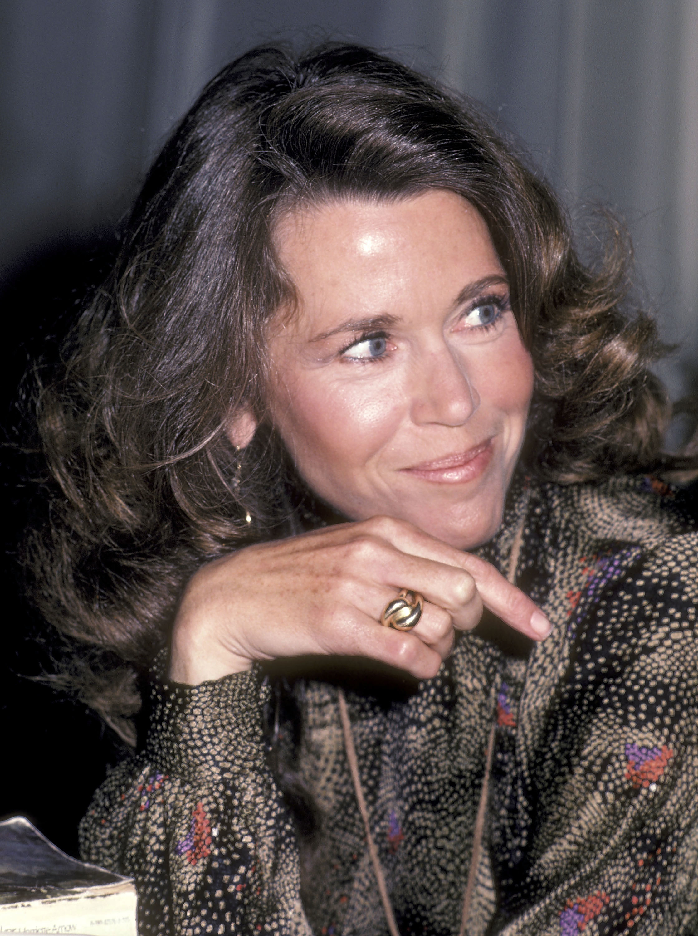 Close-up of Jane smiling with her chin resting on her hand, wearing a patterned top