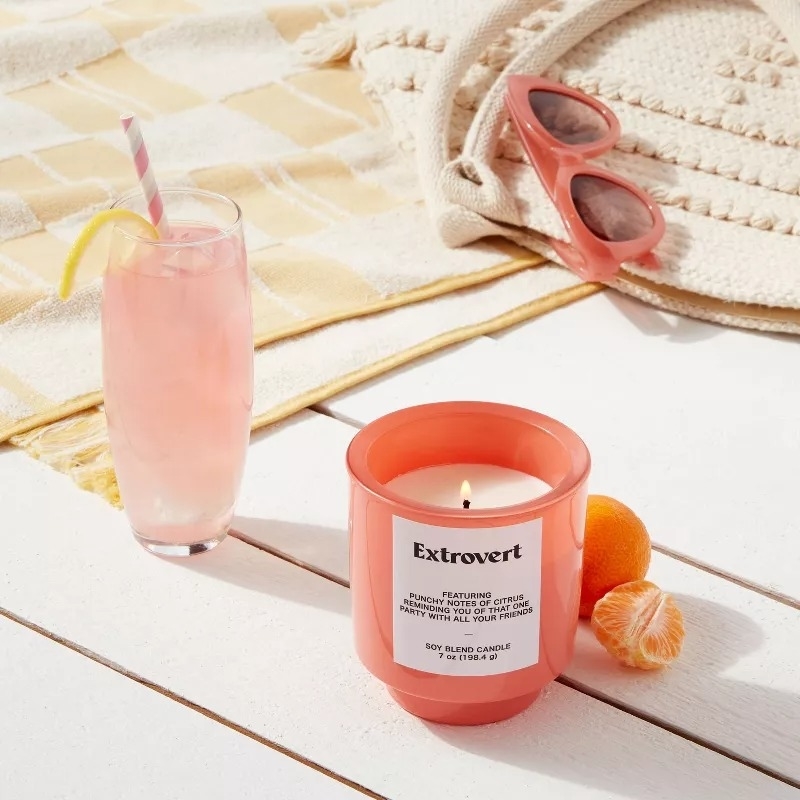 A lit &quot;Extrovert&quot; candle in a peach-colored glass jar