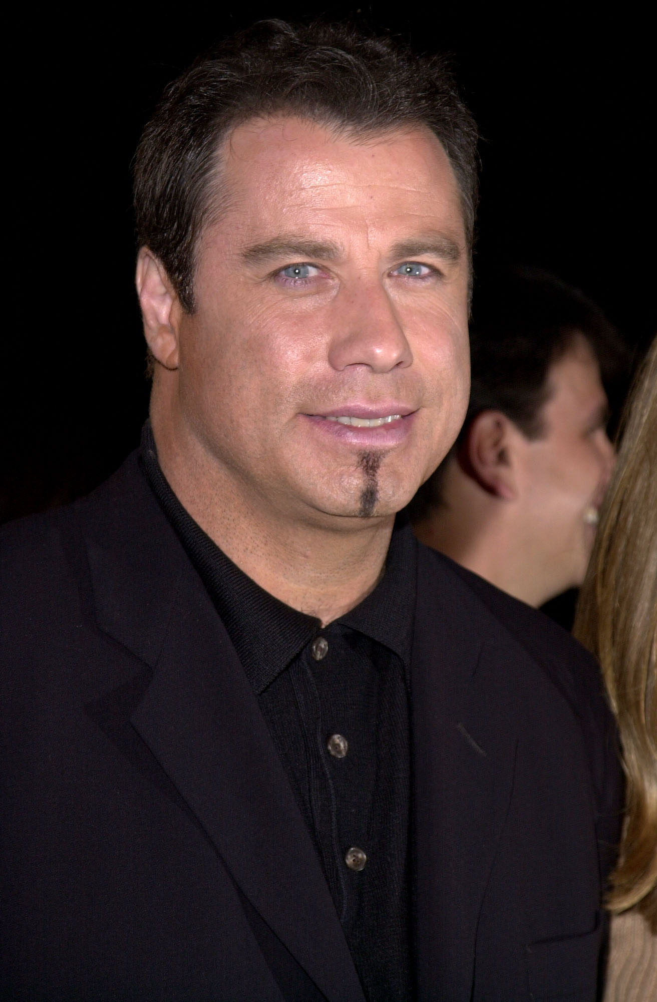 John Travolta wearing a classic black suit, attending a celebrity event