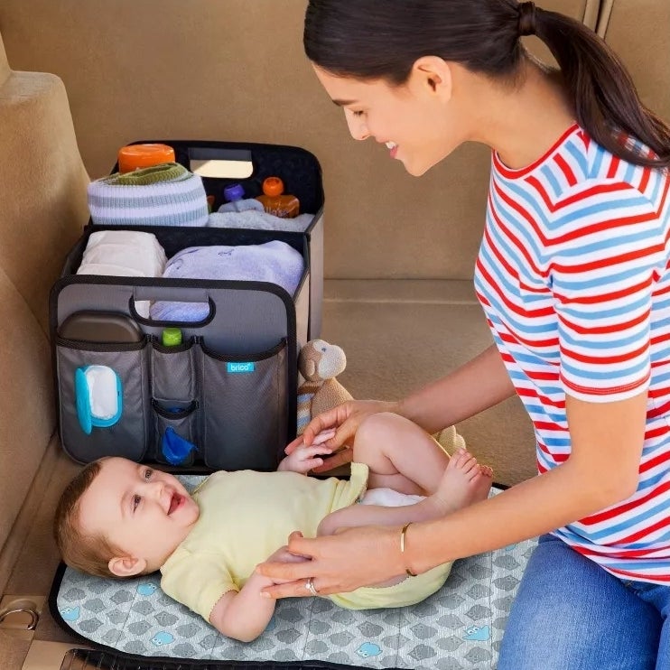 person changing baby on a portable changing pad, car organizer with supplies beside them