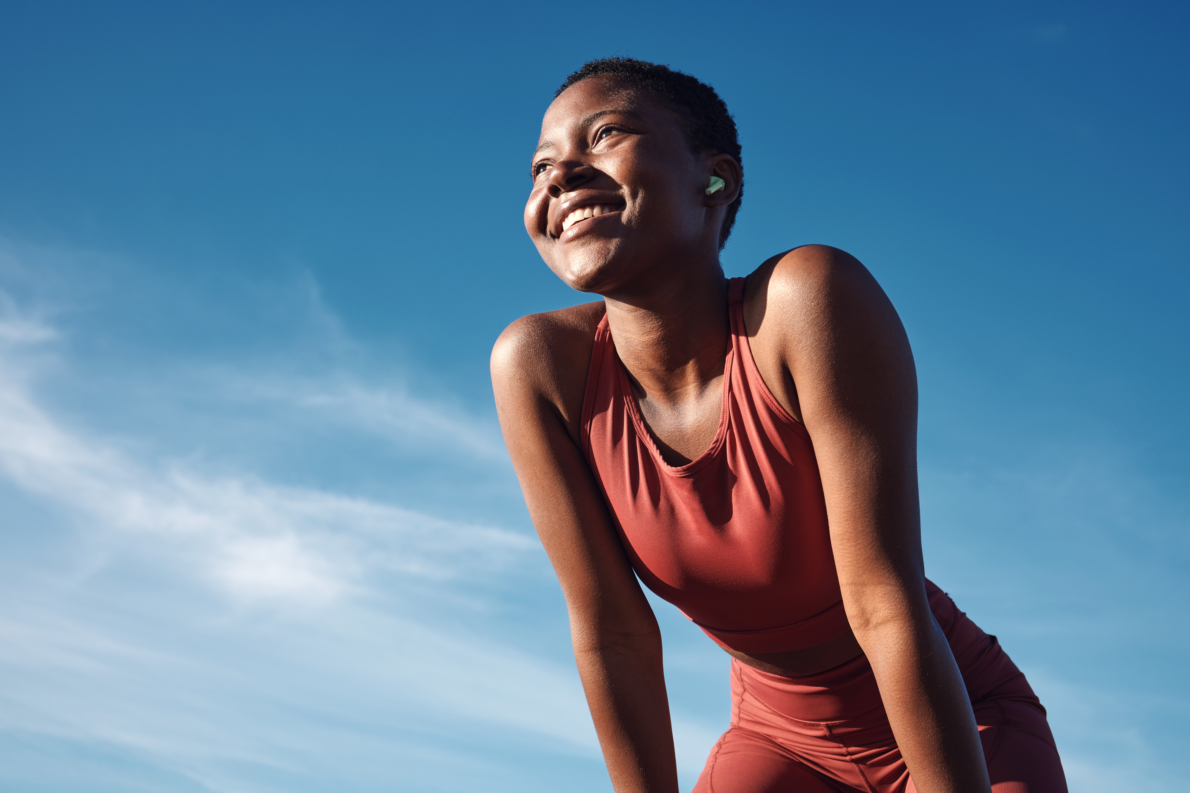 Woman in sportswear smiling against sky, possibly post-exercise, reflecting resilience and joy in fitness journey