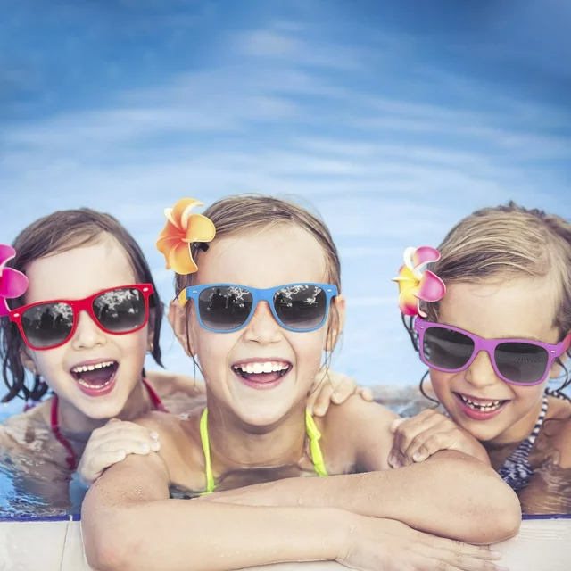 Three kids with sunglasses and floral hair accessories smile in a pool