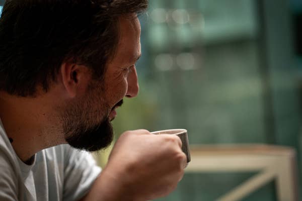 Man smiling gently while holding a mug, suggestive of warmth or contemplation
