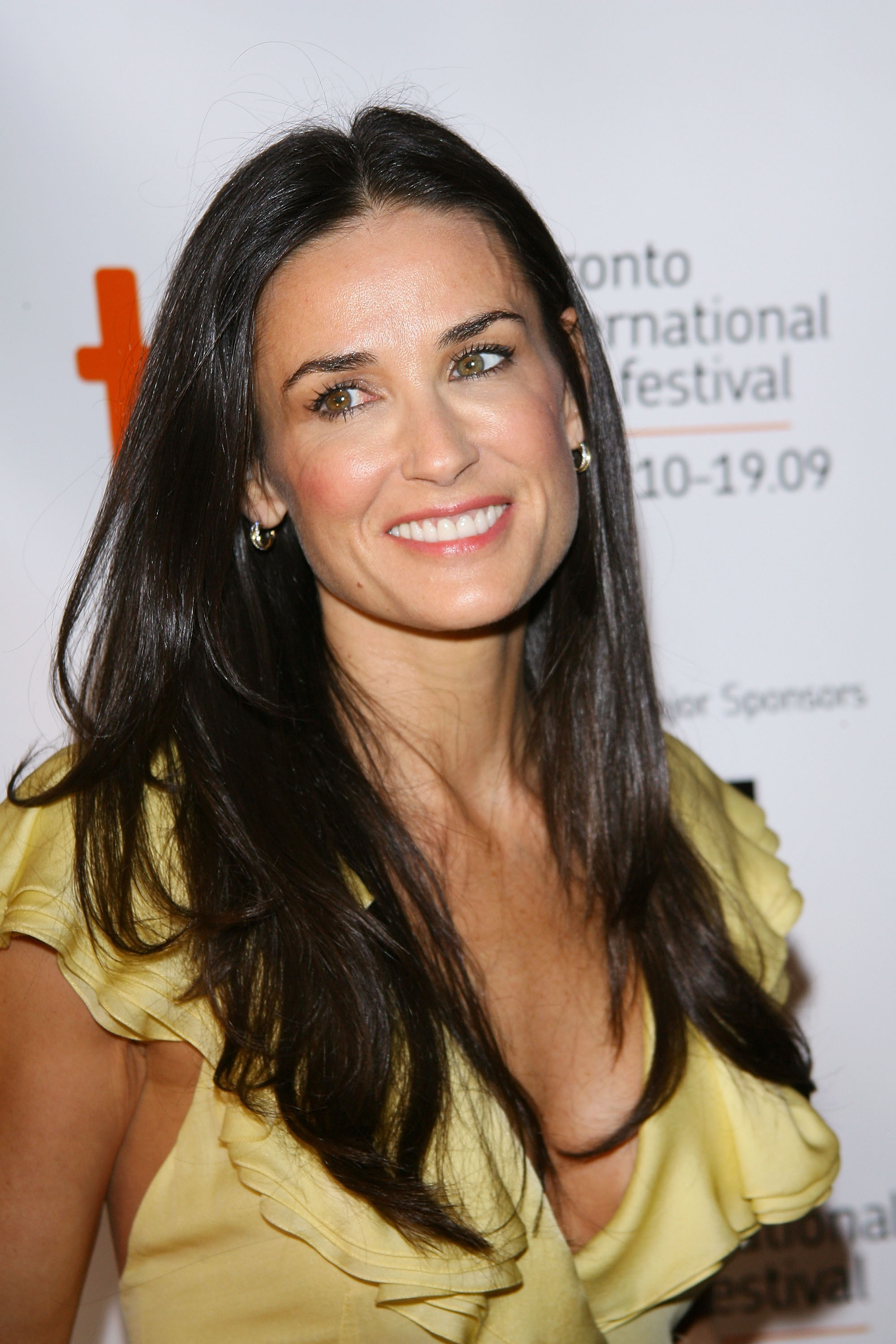 Demi Moore smiles at an event wearing a ruffled yellow top and earrings