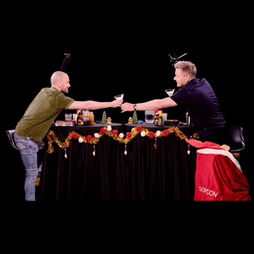 Two men engaging in a mock arm-wrestling battle across a table decorated for the holidays