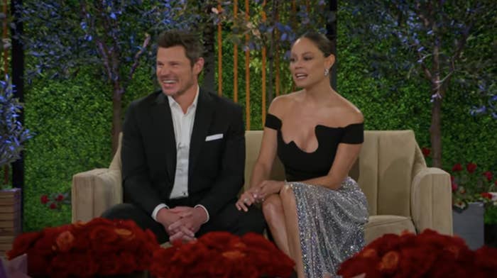 Nick and Vanessa are seated together, Nick is on the left in a suit and Vanessa is on the right in an off-shoulder top and sequined skirt