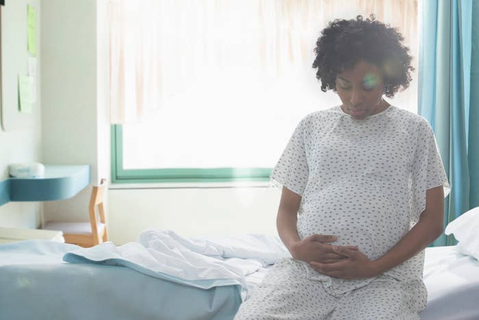 Pregnant woman sitting on a hospital bed, holding her belly, looking down