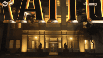 Animated sign of "THE TRAITORS" above the entrance of an illuminated building at night