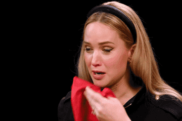 Woman appearing distressed, wiping her nose with a tissue, wearing a headband and dark top