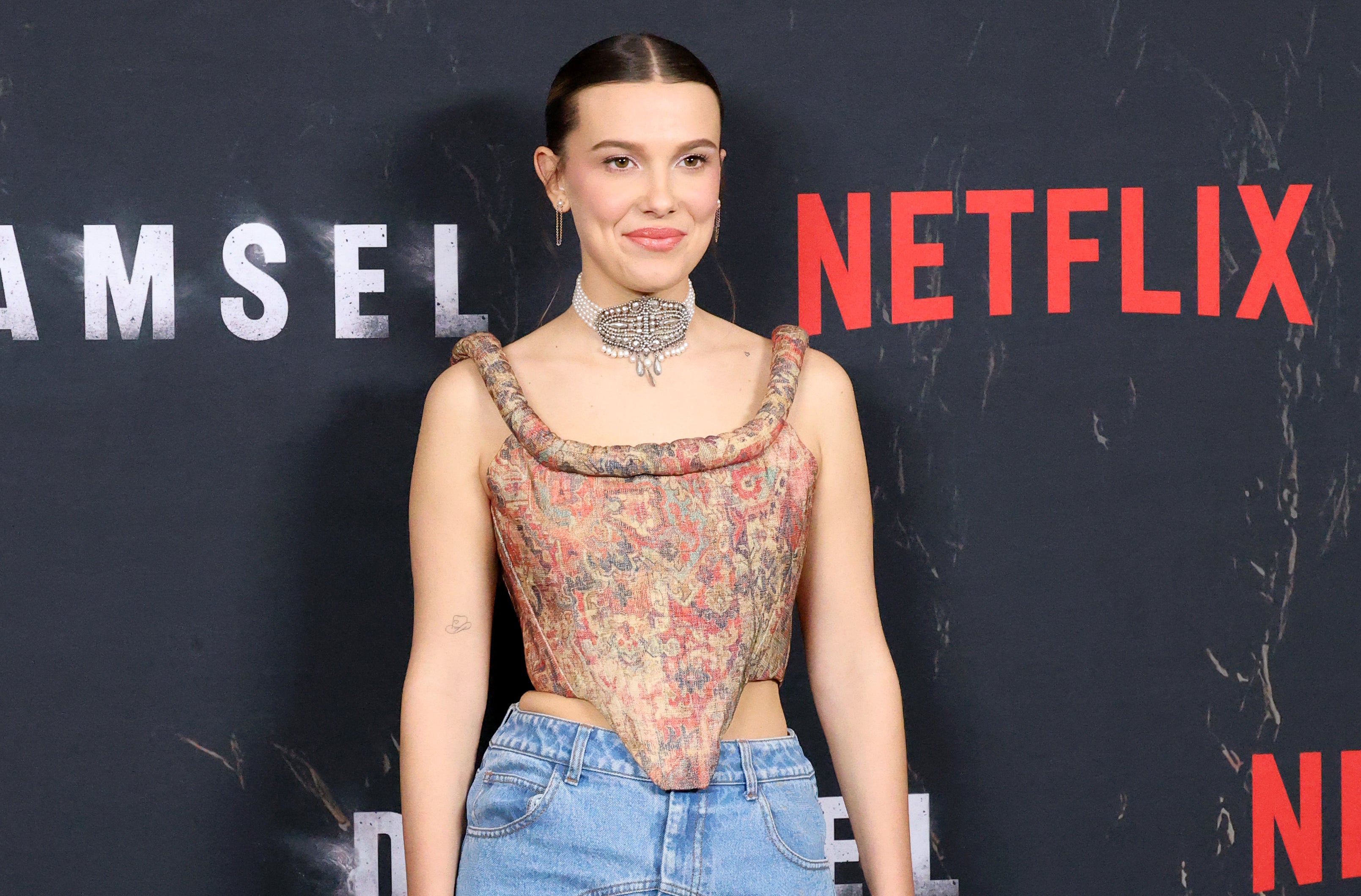 Millie Bobby Brown in patterned corset top and jeans posing at &#x27;Damsel&#x27; Netflix event