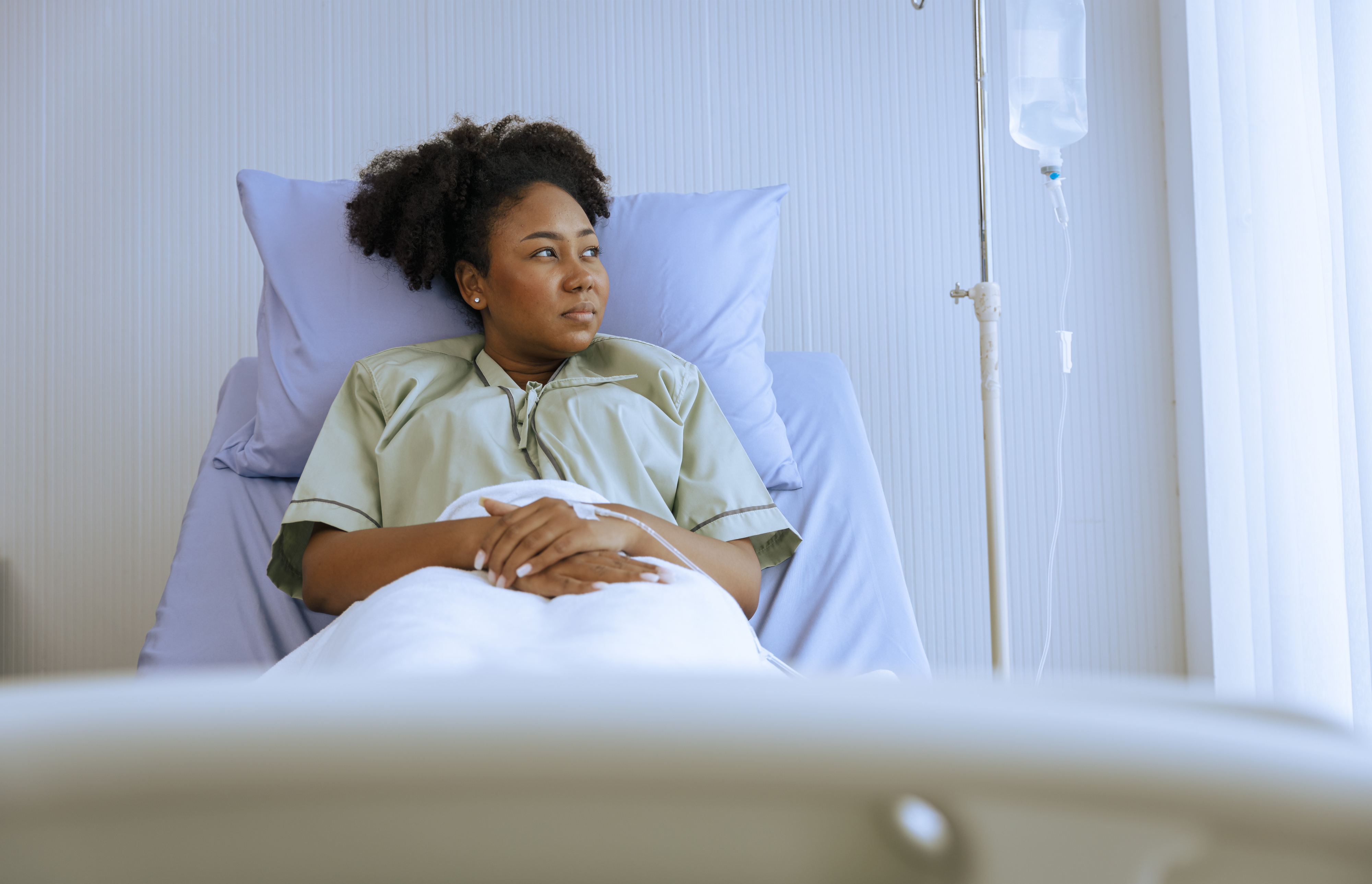 Woman in a hospital bed looking to the side with an IV stand in the background