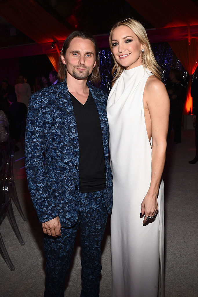 Matthew in a patterned suit and Kate in a white sleeveless gown standing together