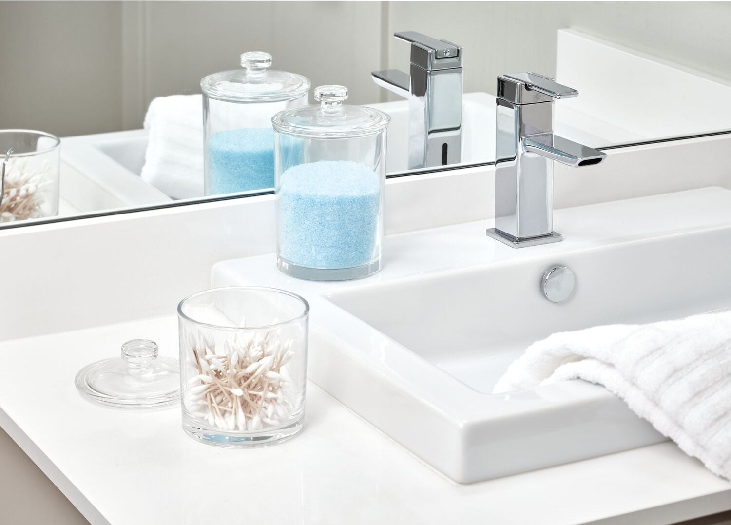Bathroom sink with glass jars containing bath products and a white towel