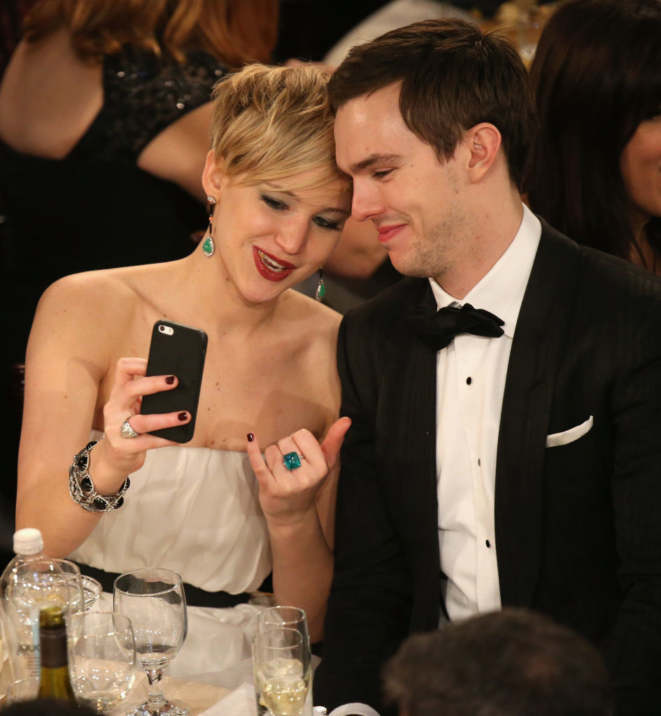 JLaw showing something on a smartphone to Nicholas; both appear engaged and smiling