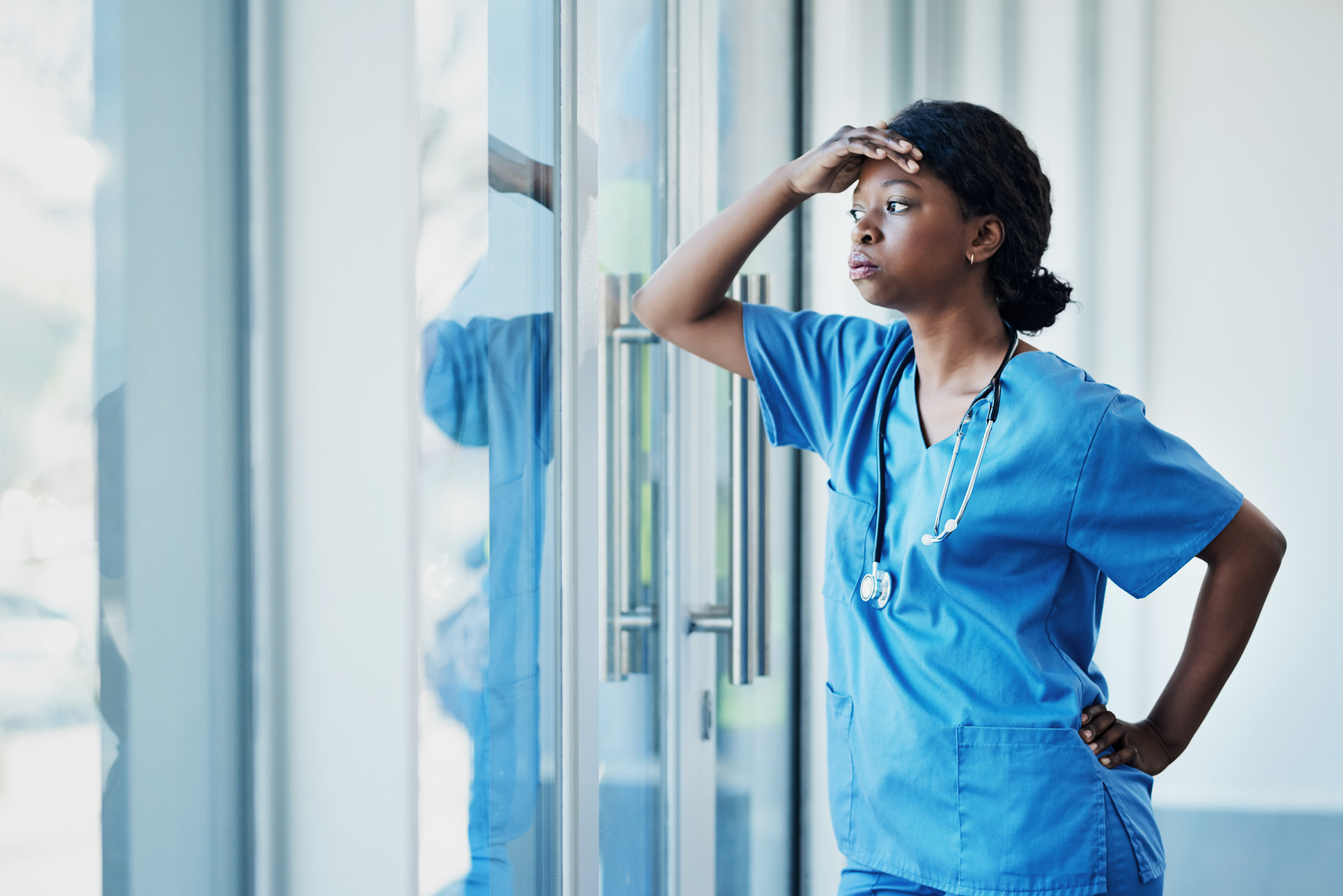 Healthcare professional in scrubs looking out the window with a thoughtful expression