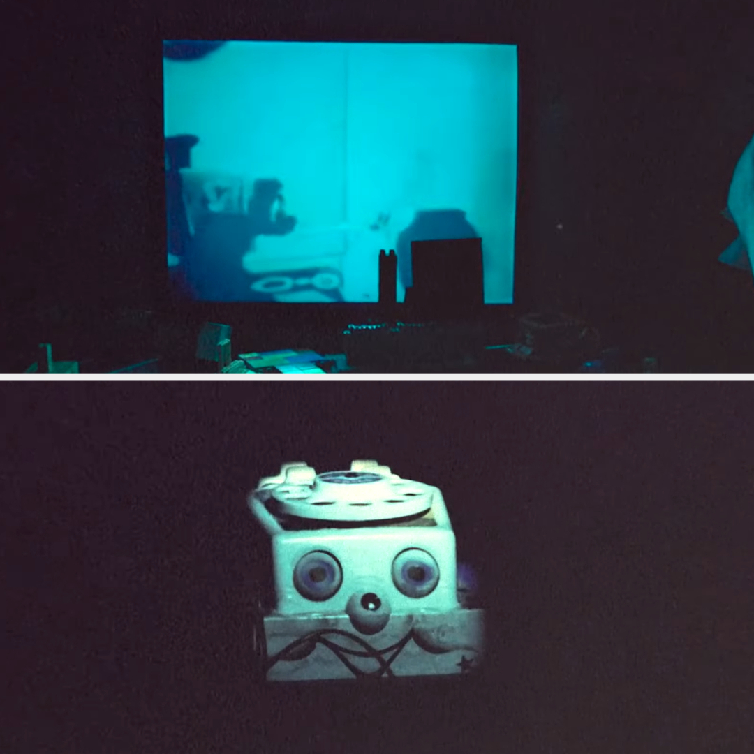 Projected image on a wall above a whimsical face made of assorted objects on a surface