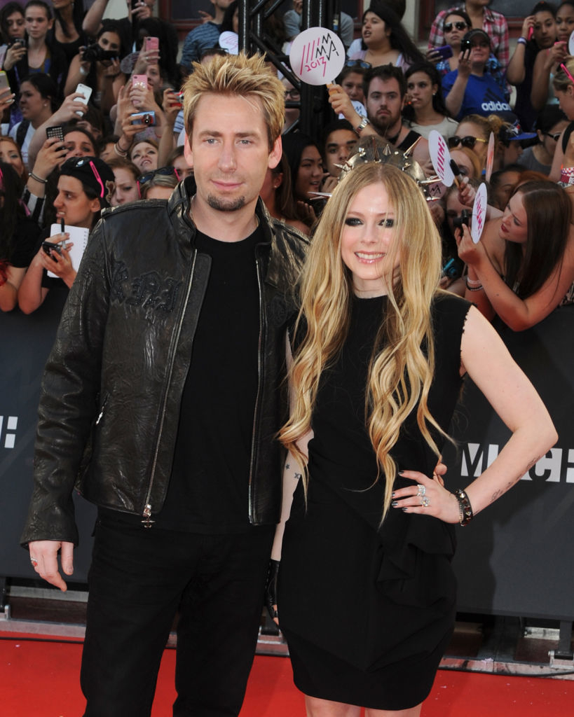 The pair posing on the red carpet, Chad in a black leather jacket and Avril in a ruffled black dress, with fans in the background