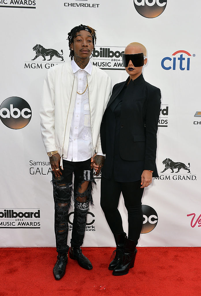 The two holding hands at the Billboard Music Awards; Wiz in a white jacket and ripped jeans, Amber in a black pantsuit and oversize sunglasses
