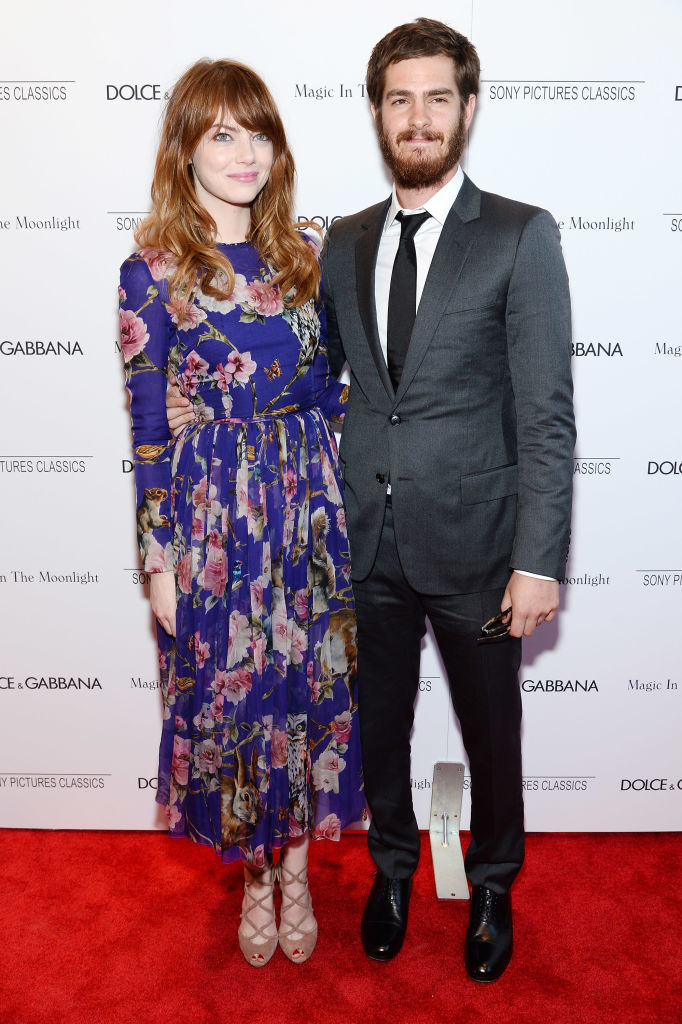 On the red carpet, Emma wears a long floral dress and Andrew in a gray suit and tie, both smiling