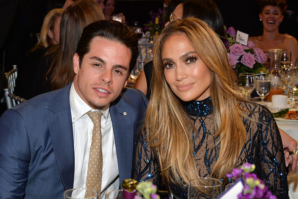 The two sitting at a table during an event, Casper wearing a suit and JLo in a beaded dress