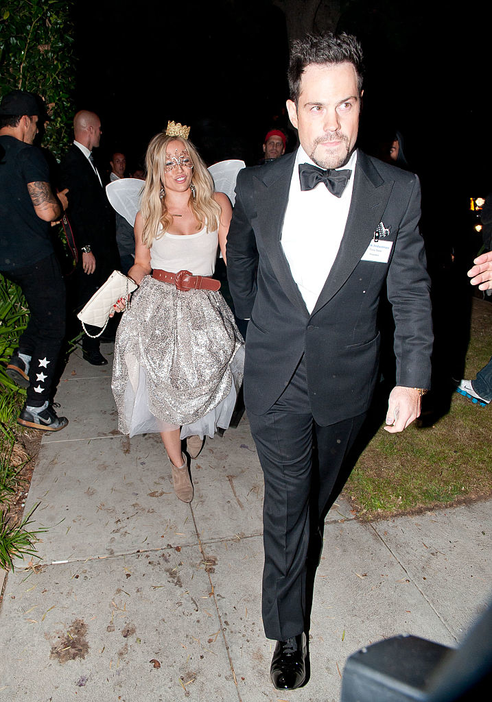 Hilary in a fairy outfit with wings and small crown, Mike in a tuxedo and bow tie, walking outdoors at night