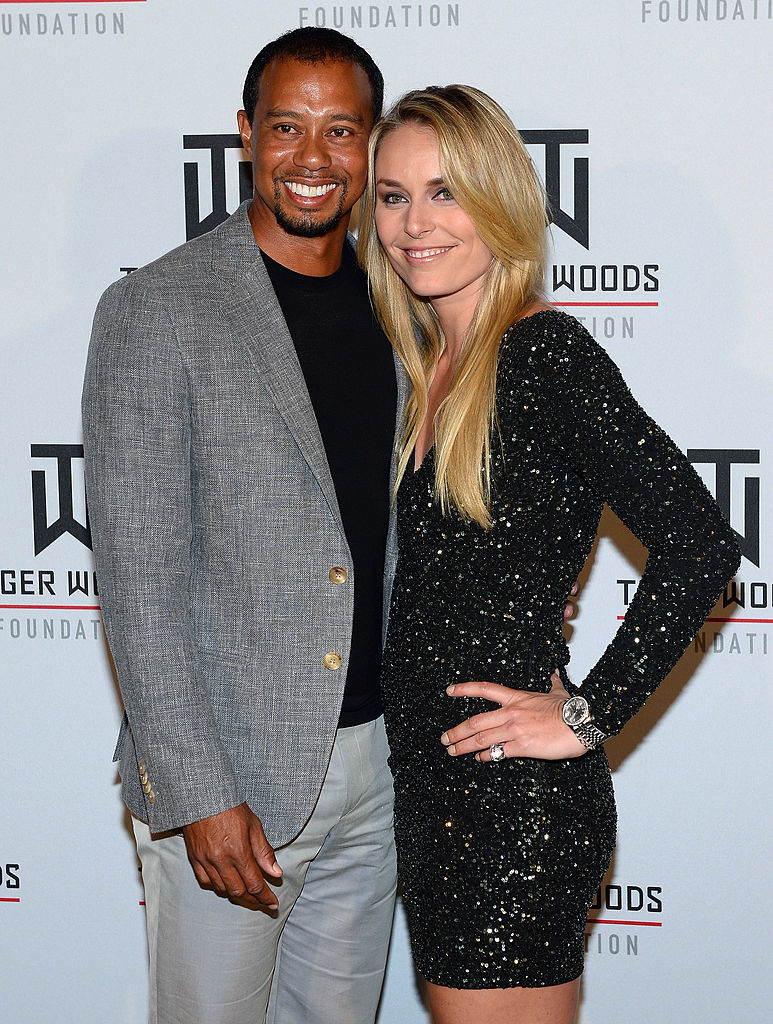 Tiger Woods in a gray blazer with Lindsey Vonn in a black sequined dress, both smiling at a foundation event