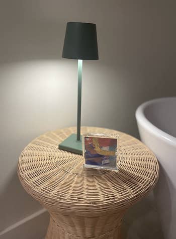 A modern table lamp on a wicker stand, with a decorative item beside it, in a home interior setup