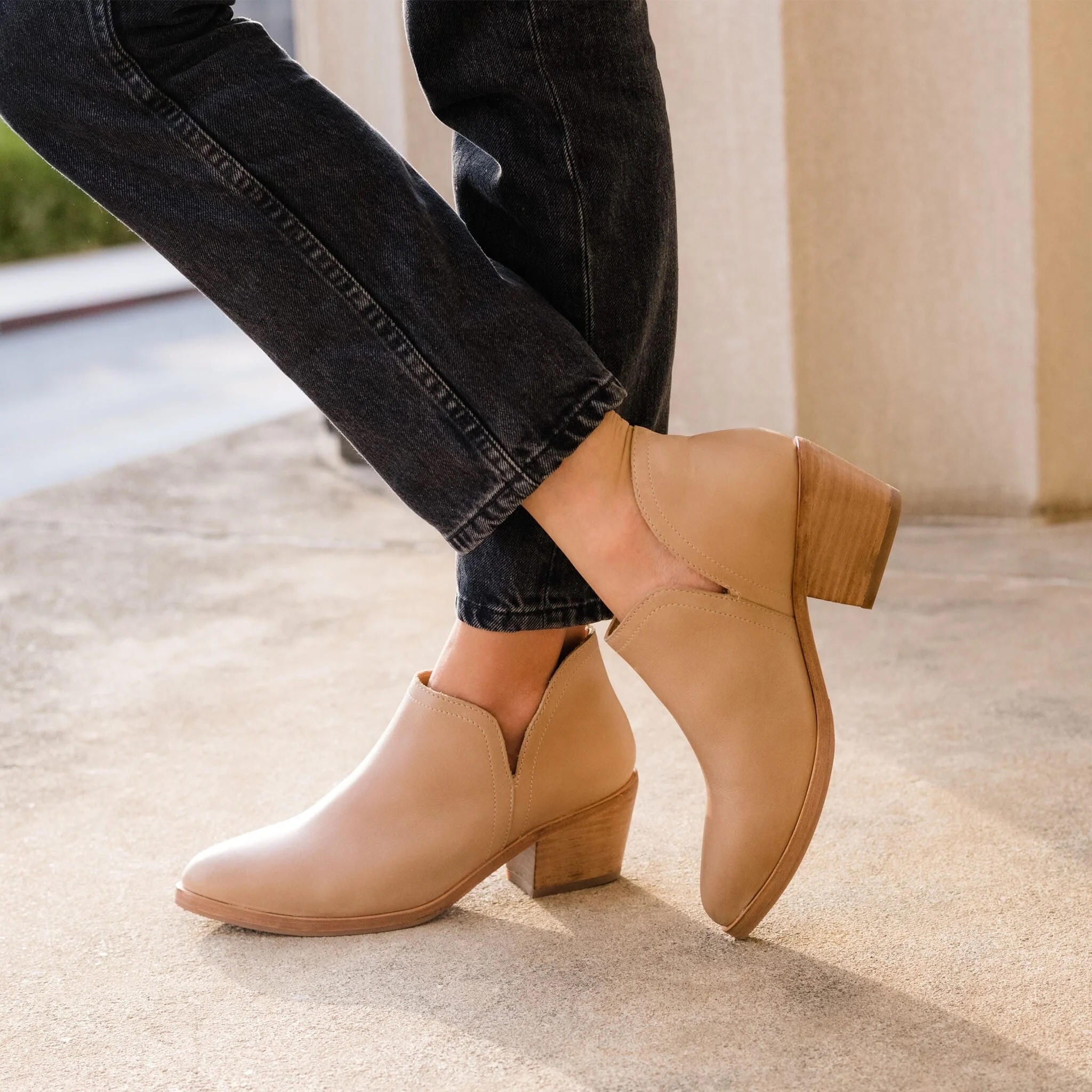 Person wearing beige ankle boots with elastic side panels and wooden block heels, paired with black jeans
