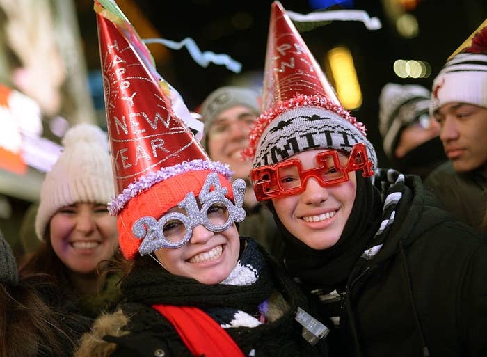 Two people wearing festive &quot;Happy New Year&quot; hats and 2014 glasses celebrating