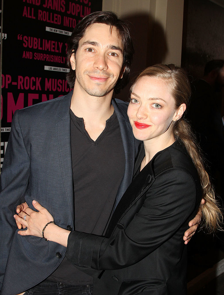 The pair smiling and embracing at an event, Justin wearing a black suit and Amanda in a dark blazer