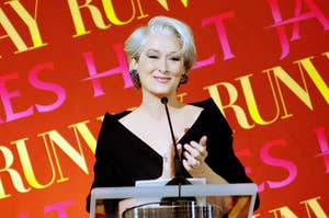 Meryl Streep speaks at a podium, wearing an off-shoulder gown with a smile