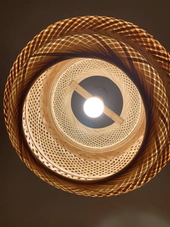Woven pendant lamp hangs from ceiling, pattern casts spiraling shadows