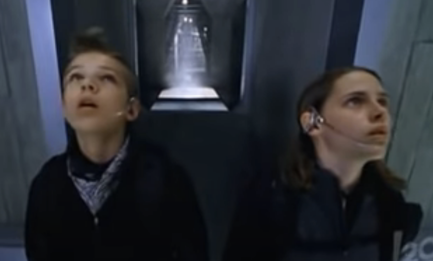 Two children look upwards with awe inside a sci-fi corridor